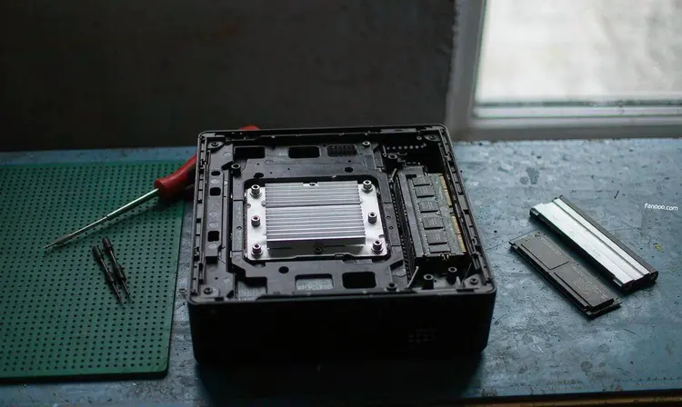 工作台上拆开的小型主机机箱,旁边放着一条笔记本内存和一块 NVMe 固态硬盘,还有一把小螺丝刀